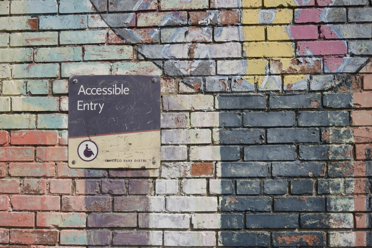 An old brick wall showing signs of old paint has a battered sign on it that says Accessible Entrance.