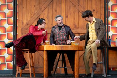 Three men sitting at a table in front of a stable door in a production of 'The Merry Wives of Windsor.'