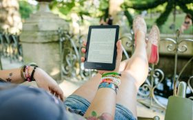 Photo cropped so it's overlooking the shoulders of a person holding a kobo ereader with legs outstreched in a relaxing outdoor environment. People read the most in January.