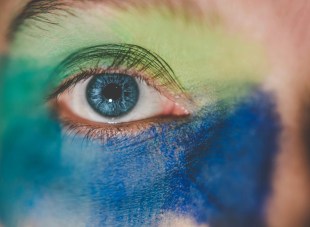 Detail of a painted face and eye in blues and greens. Arts news