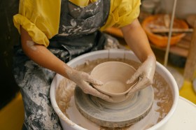 Woman in yellow shirt at potters wheel. Art workshops