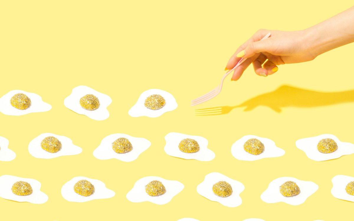 A hand poking out from the right hand side holding a fork, about to lift up a sunny side egg with a sparkly gold yolk. There are three rows of sunny side eggs lined up against a yellow background.