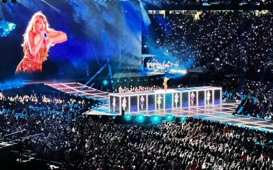 More international concerts will tour to Australia in 2025 thanks to the success of Taylor Swift's Eras Tour. A photo of the concert with a massive crowd as Swift is pictured standing on top of an elevated stage and a big screen showing her singing up close.