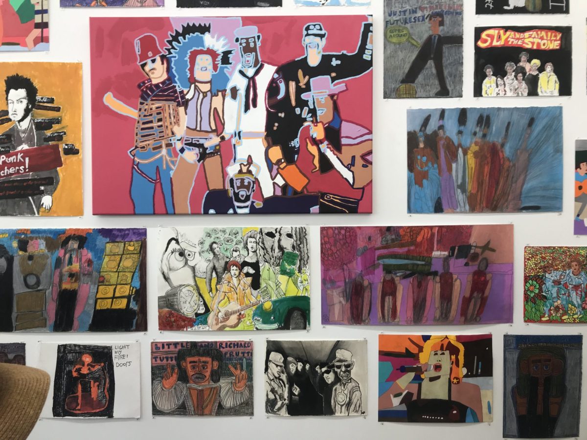 A selection of colourful artwork hung closely to one another on a white wall.