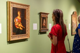 woman in red dress looking at medieval portrait in gallery with green walls. Abbey Museum