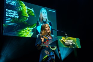 Woman accepting award standing at a lectern and video screen behind. APRA Art Music Awards