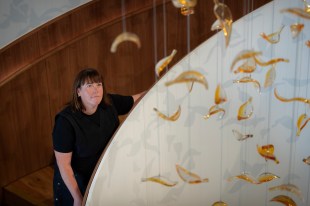 Woman in black top with dark hair looking at floating sculpture of glass leaves. Annette Blair