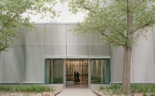 The entrance of TarraWarra Museum of Art's new Eva and Marc Besen Centre, designed by Kerstin Thompson Architects. A rectangular steel structure framed by green leafy branches with an entrance way into a contemporary education and visible storage centre.