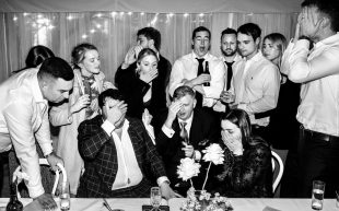 A black and white photo of a group of people dressed in formal suits and dresses at a party, looking comically devastated.