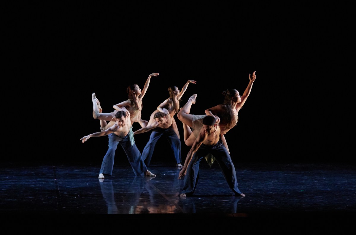 Six dancers in formation. The bare-chested men in black pants are balancing the women on their backs.