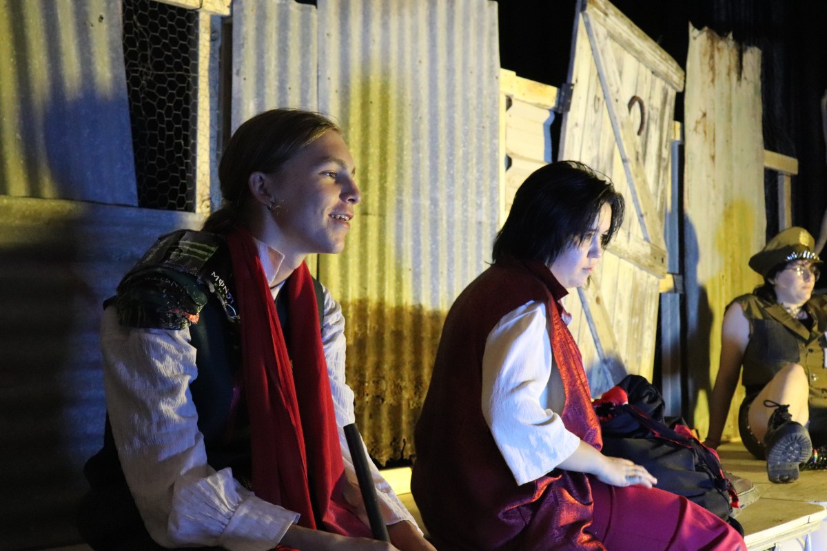 Two young actors in red and white sit on stage facing and looking right. War of the Worlds.