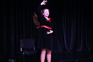 A young woman wearing a black dress with red trim has one arm over her head and one by her stomach.