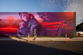 Man walking past a large street art mural at dusk. Wall to Wall festival