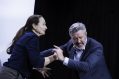 Caroline Lee, with brown hair in pony tail and wearing blue top, is tussling with Peter Houghton, a man with grey hair in a suit. Honour.