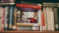 A man and a woman's partial faces can be seen through a tower of books.