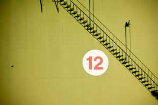 The number twelve in red and white against a yellow wall with a diagonal