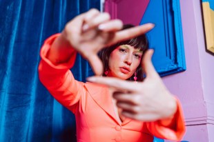 Young woman in orange outfit holding up fingers and looking through them. Event trends