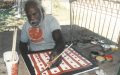 Midpul, a First Nations male Elder, sitting and painting with a brush, making lines and dots in ochre.