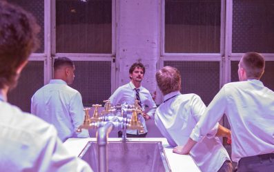 Five schoolboys in white shirts gather around a water trough.