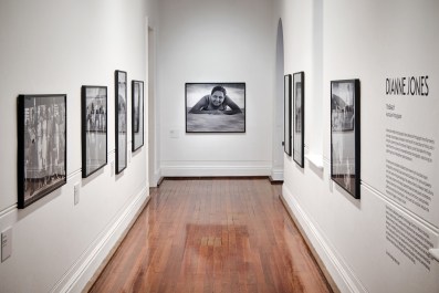 A white gallery space with black and white photographs along the walls and a shiny wooden floor. Dianne Jones