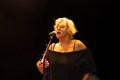 A woman in a shoulder less black top with short bleached hair sings in to a microphone. She looks a little tortured. Cat Power. Port Fairy Folk Festival.