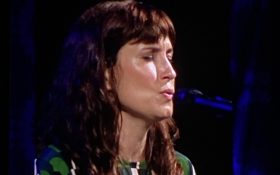 A woman with longish dark brown hair and a green, white and black dress, sings into a mic with her eyes closed. Missy Higgins. Port Fairy Folk Festival.