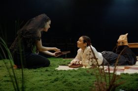 A woman in black is crouched over talking to a woman on the grass.