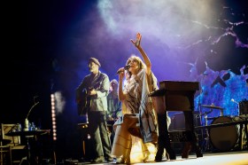 women with dark hair and white dress expressively performing on stage. PJ Harvey