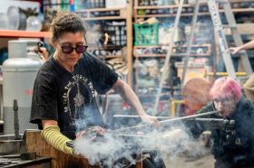 Woman with dark hair seated on bench makingglass art.