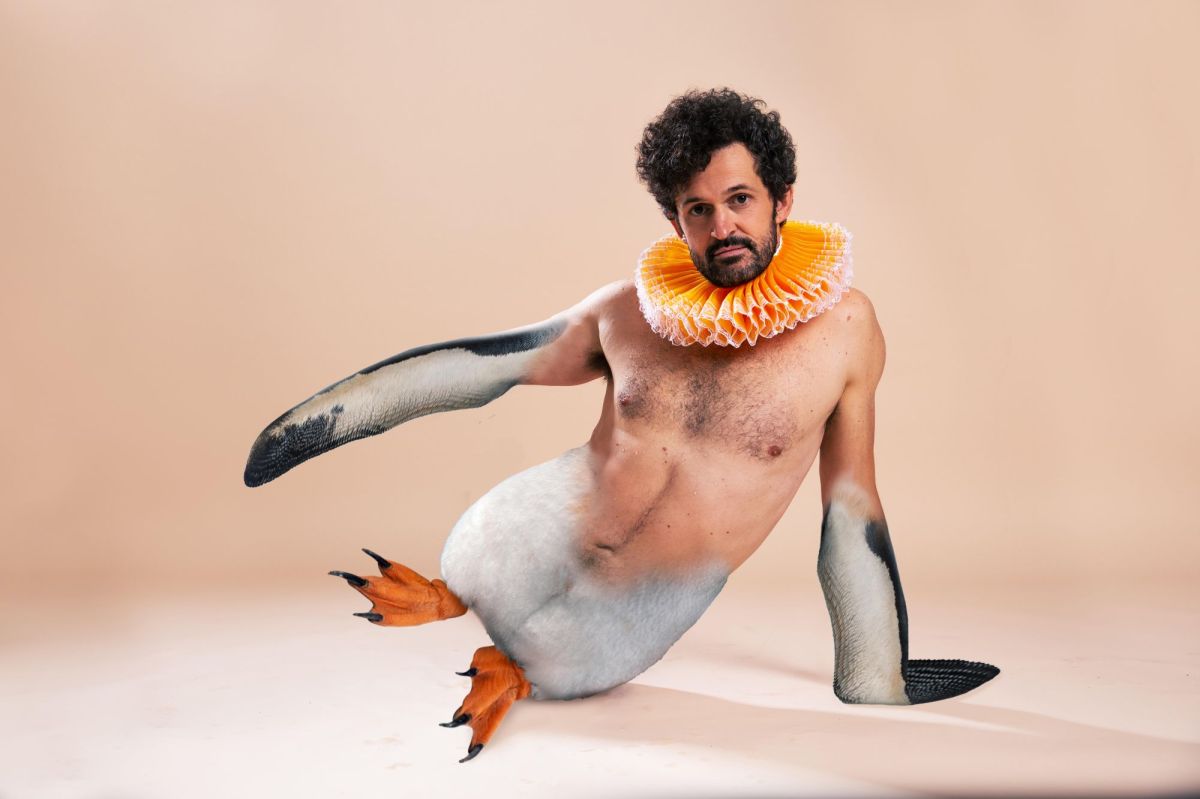 'Garry Starr: Classic Penguins' at The Garden of Unearthly Delights, Adelaide Fringe 2025. A photoshopped image of a fair-skinned man with curly black hair and a neat beard wearing an orange-coloured Elizabethan ruff. His arms from the elbows down, and his body from the waist down, have been photoshopped to appear like a penguin. He leans on his left flipper and sits on his left penguin hip, his orange penguin feet and right flipper raised.