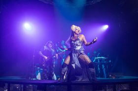 A man in drag on stage. There is a band behind him.