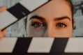 A young woman peers through the gap of a clapperboard.