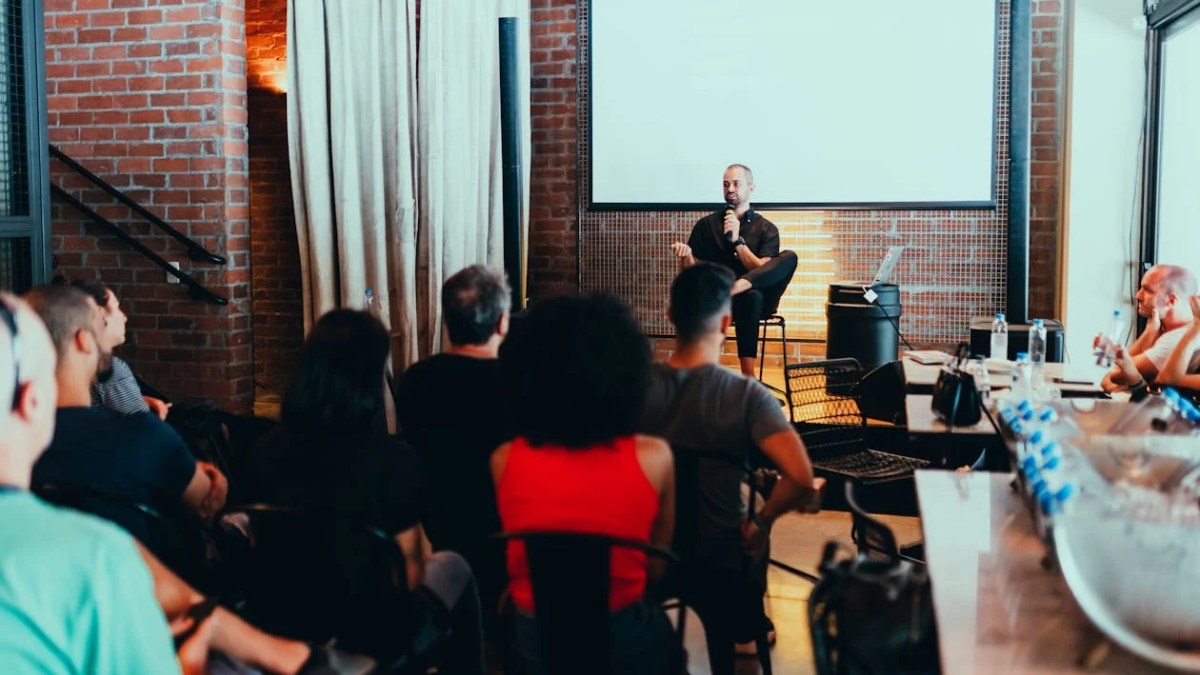 Photo of people gathering around a small stage to listen to a speaker.