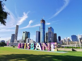 View of a city with blue sky and the word Brisbane in front. Olympics